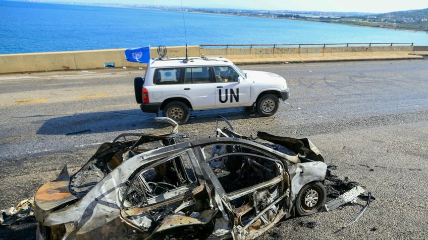 A UNIFIL (the United Nations Interim Force in Lebanon) patrol drives past the wreckage of a car 