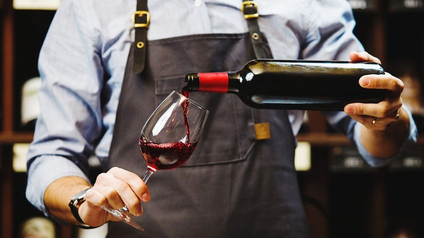 Male sommelier pouring red wine into long-stemmed wineglasses.