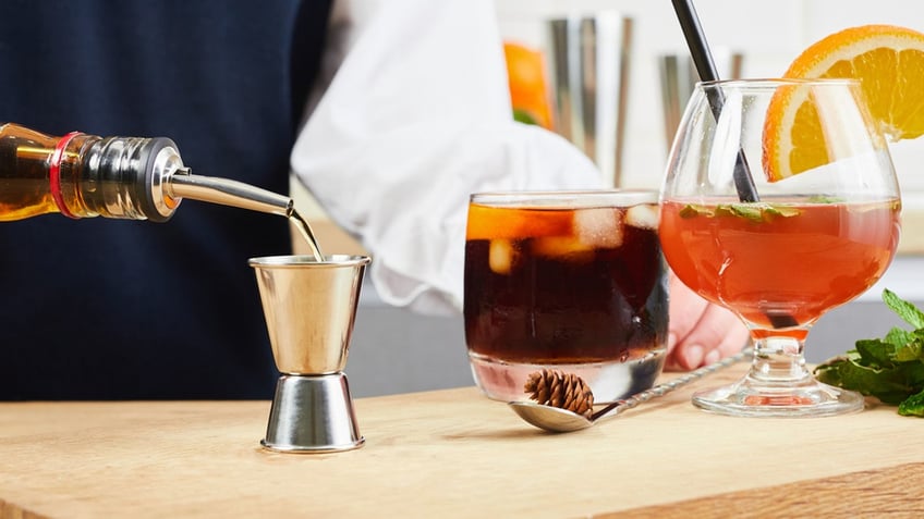 Girl prepares a cocktail using a jigger to control the amount of ingredients added to the cocktail.