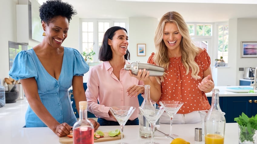 Women laugh while making cocktails at a home bar.