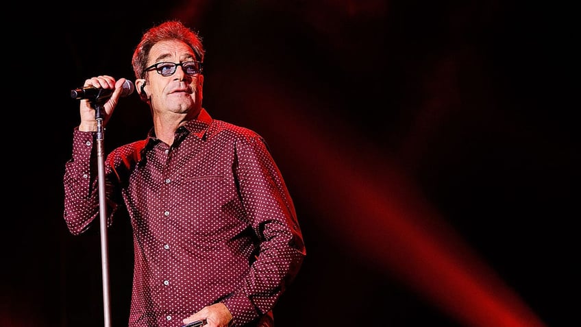 Huey Lewis standing at microphone on stage