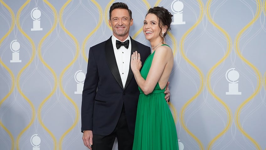 Sutton Foster wearing a green dress with her hand on Hugh Jackman's chest.