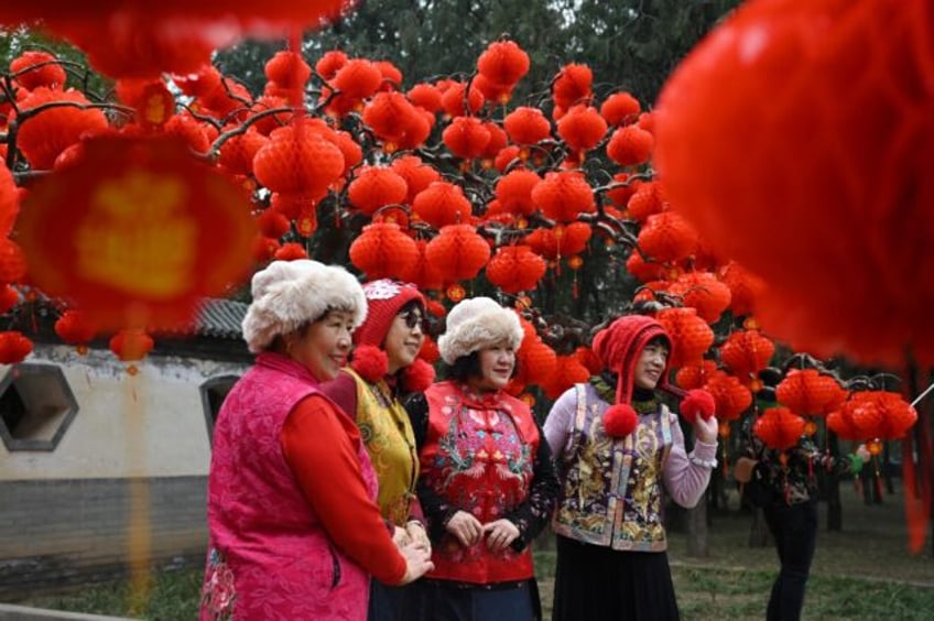 A group of women pose for photos under decorations for a temple fair ahead of Lunar New Ye