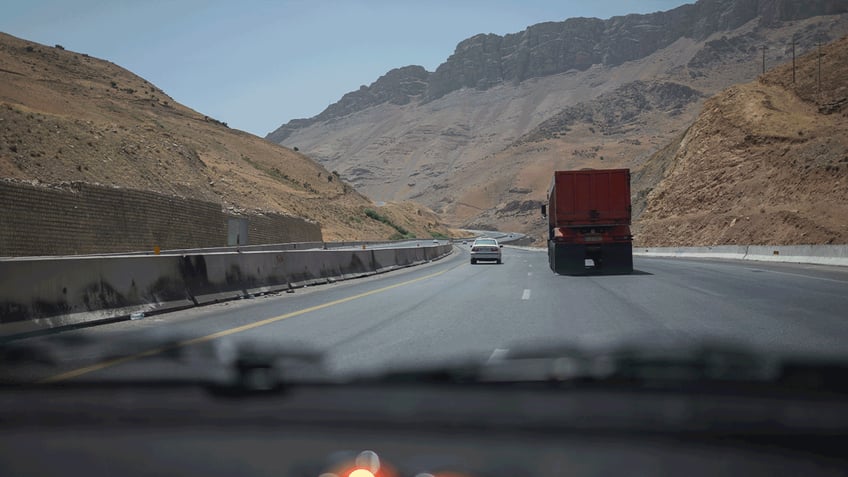 cars drive on highway through arid mountains