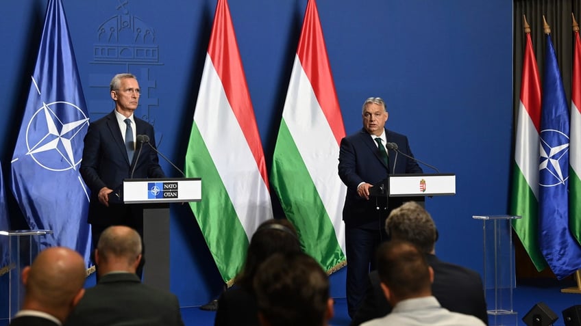 Hungarian Prime Minister Viktor Orban and NATO Secretary General Jens Stoltenberg stand at podiums in front of Hungary and NATO flags at a press conference.