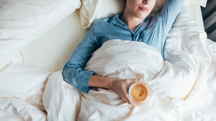 woman lying in bed holding coffee in hand.