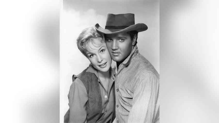 Elvis Presley in cowboy gear with his cheek against Barbara Eden.