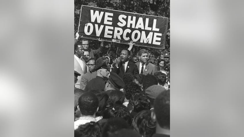 Dr King with We Shall Overcome sign