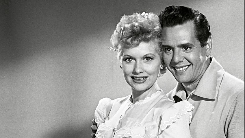Lucille Ball wearing a white nightgown leaning on her smiling husband Desi Arnaz.