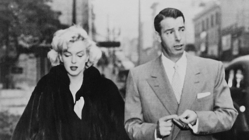 Marilyn Monroe and Joe DiMaggio walking together and looking serious.