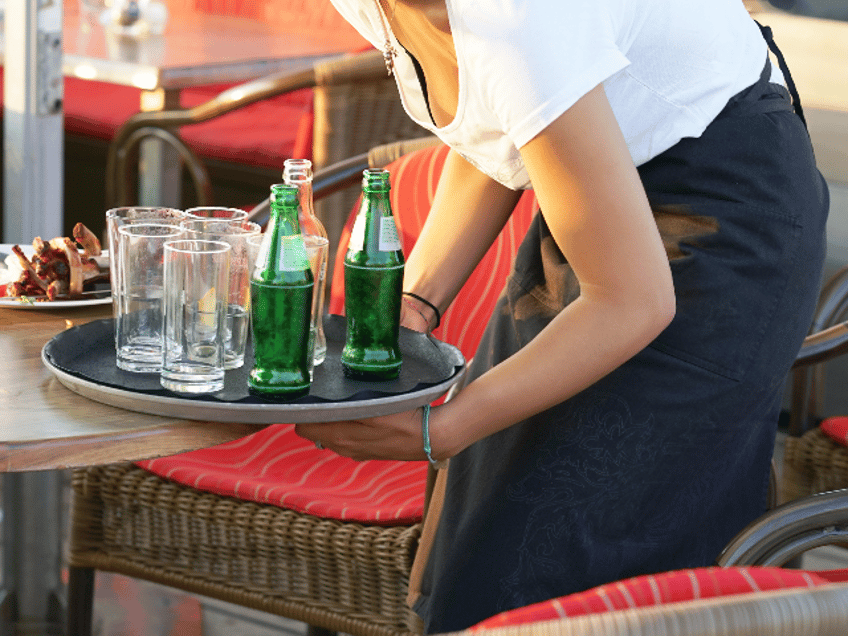 A waitress is holding a tray with dirty dishes and leftover food. Waitress cleaning the table in a restaurant. The concept of service.