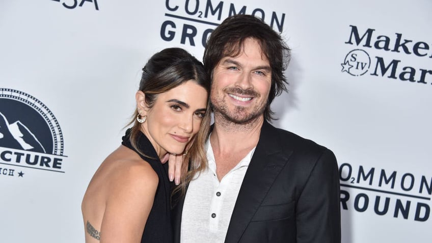 Nikki Reed in a black halter dress leans into husband Ian Somerhalder in a black jacket on the carpet