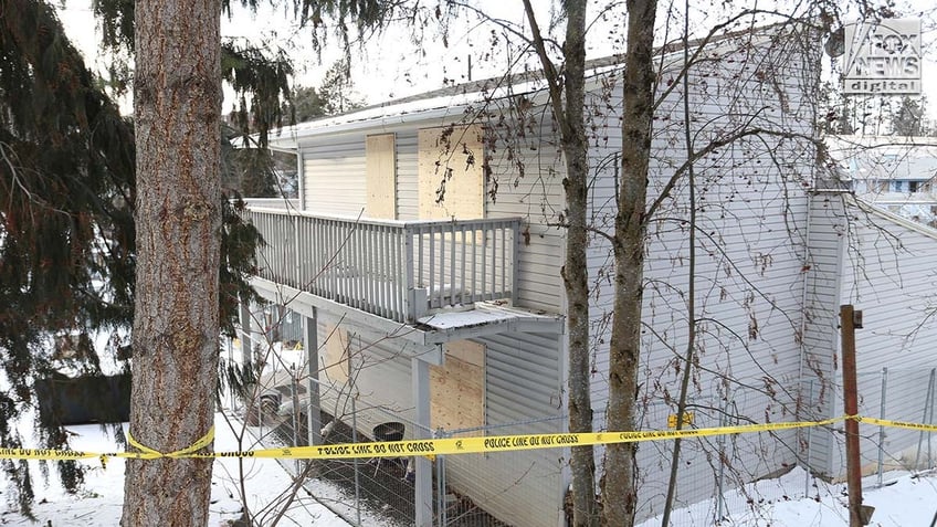 Windows on a two story house are boarded up with pieces of wood.