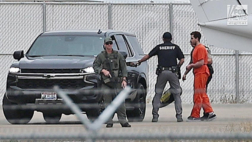 Bryan Kohberger in an orange prison jumpsuit ias led to a black SUV on an airport tarmac