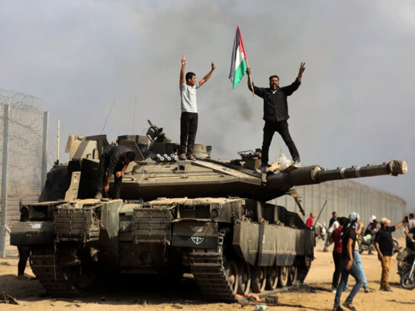 Palestinians wave their national flag and celebrate by a destroyed Israeli tank at the Gaza Strip fence east of Khan Younis southern Saturday, Oct. 7, 2023. The militant Hamas rulers of the Gaza Strip carried out an unprecedented, multi-front attack on Israel at daybreak Saturday, firing thousands of rockets as …