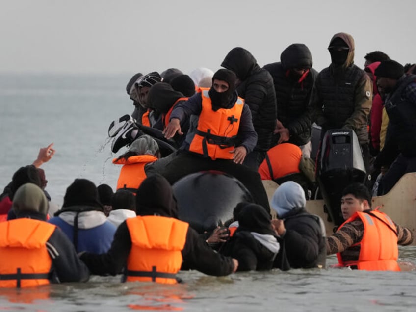 People thought to be migrants wade through the sea to board a small boat leaving the beach