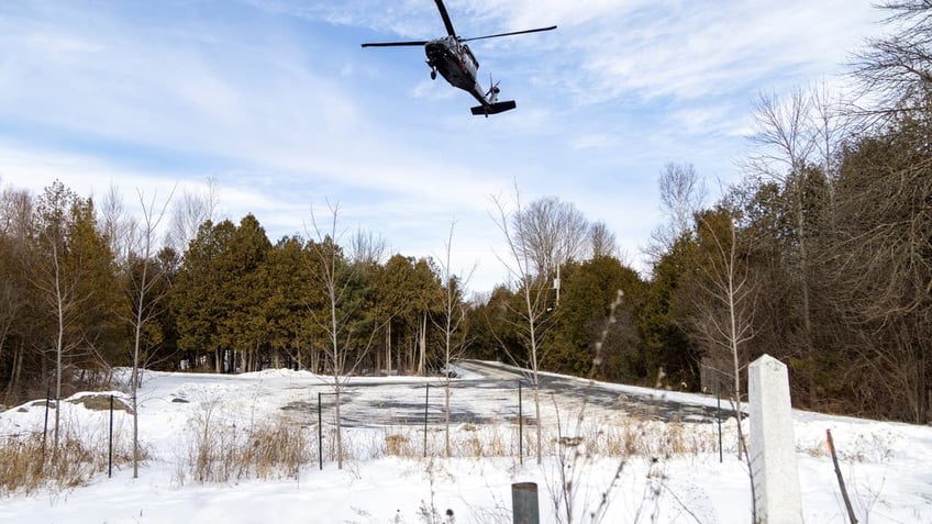 A Royal Canadian Mounted Police Blackhawk helicopter flies above US-Canada border marker with snow on the ground