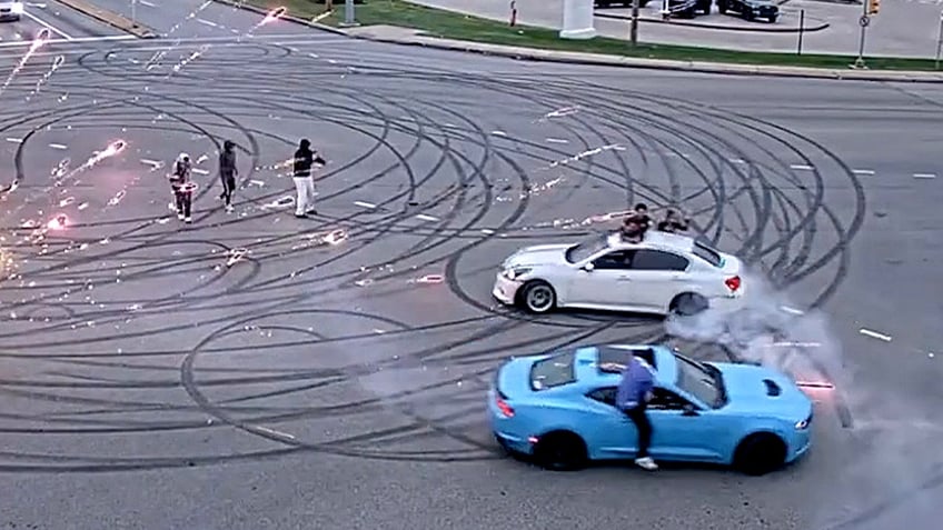 blue and white cars make donuts in large street intersection