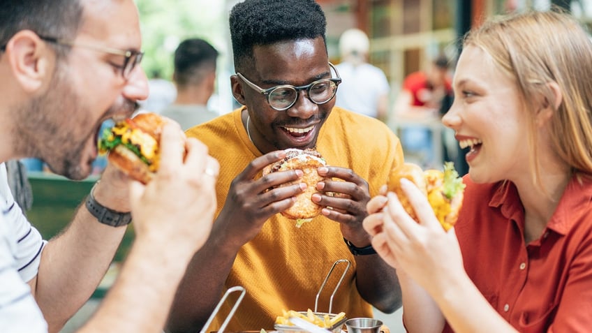 Friends eating burgers and fries at an outdoor restaurant.