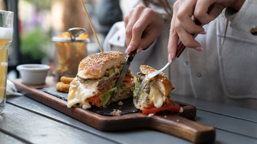 Person eating a burger with fork and knife.