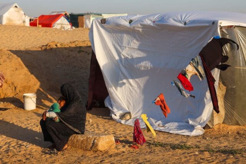 A displaced Palestinian woman cuddles her baby near her tent at a camp in Rafah on March 1