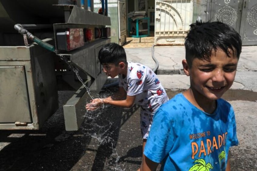 Boys cool off with water from a mobile tanker as summer temperatures soar in Iraq's northe