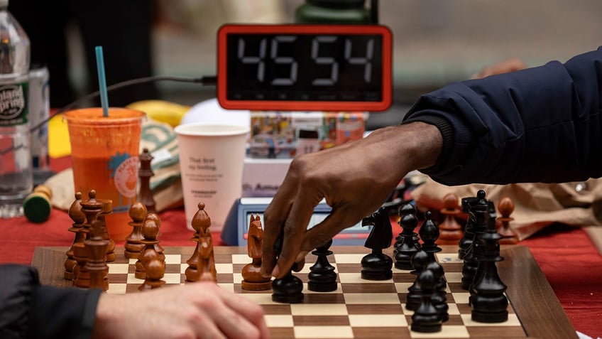 two hands playing chess in front of a clock
