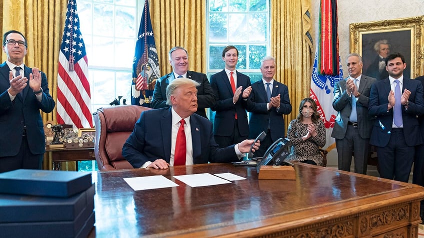 President Donald Trump hangs up a phone call with the leaders of Sudan and Israel, as Treasury Secretary Steven Mnuchin, left, Secretary of State Mike Pompeo, White House senior adviser Jared Kushner, National Security Adviser Robert O'Brien, and others applaud in the Oval Office of the White House, Friday, Oct. 23, 2020.