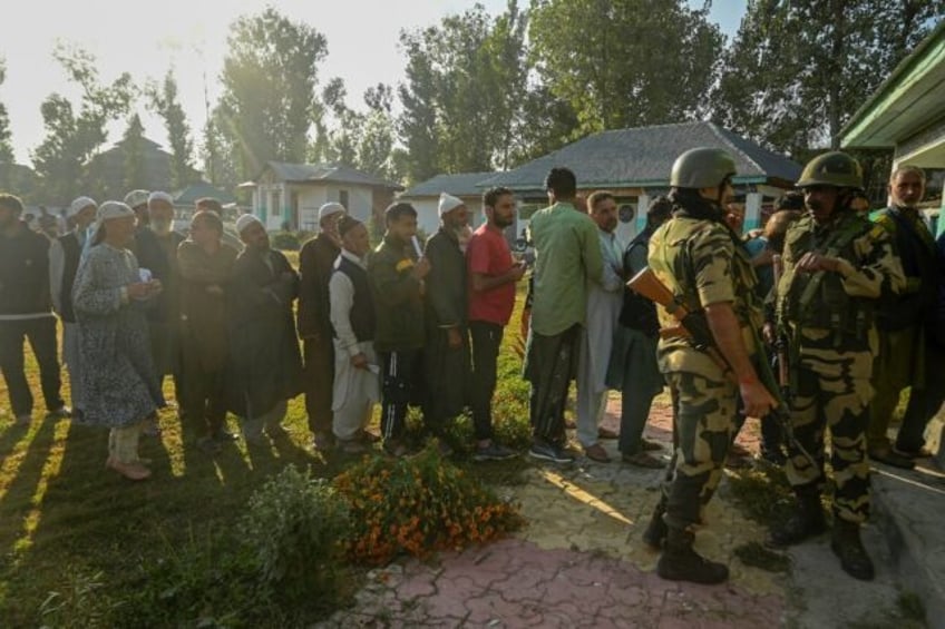Indian security personnel stand guard as voters queue up to cast their ballots at a pollin