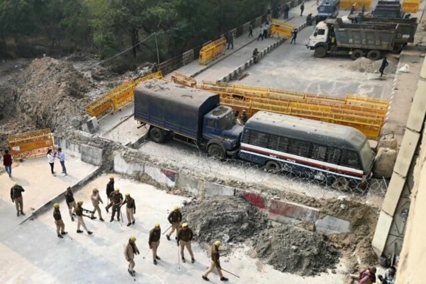 Police guard a barrier blocking a road to prevent farmers demanding minimum crop prices fr