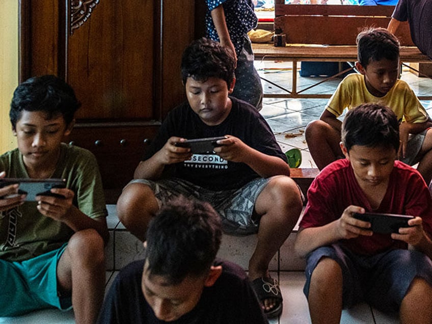 Children play with their mobile phones as a wayang kulit performance takes place prior to