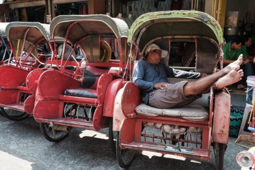 The driver of an Indonesian bechak, a traditional pedicap, sleeps in front of a market in