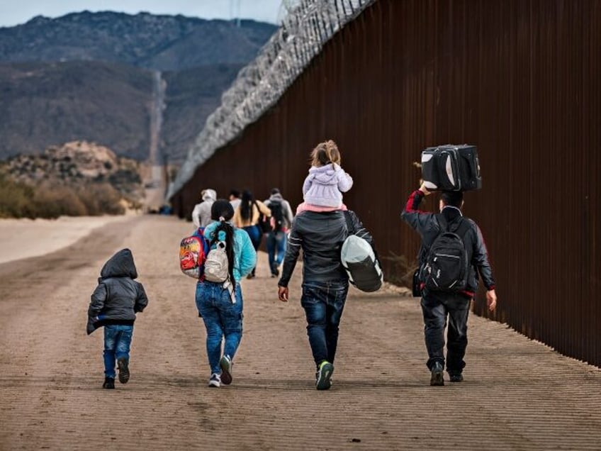 SAN DIEGO, CA - NOVEMBER 30: Asylum seekers walk along the U.S.-Mexico border barrier on their way to be processed by U.S. Border Patrol agents on November 30, 2023 in San Diego, California. (Photo by Qian Weizhong/VCG via Getty Images)