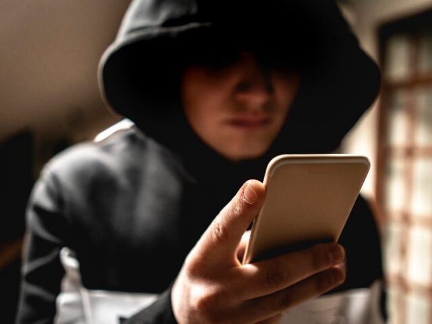 male hacker in the hood using a mobile phone, stealing your personal data