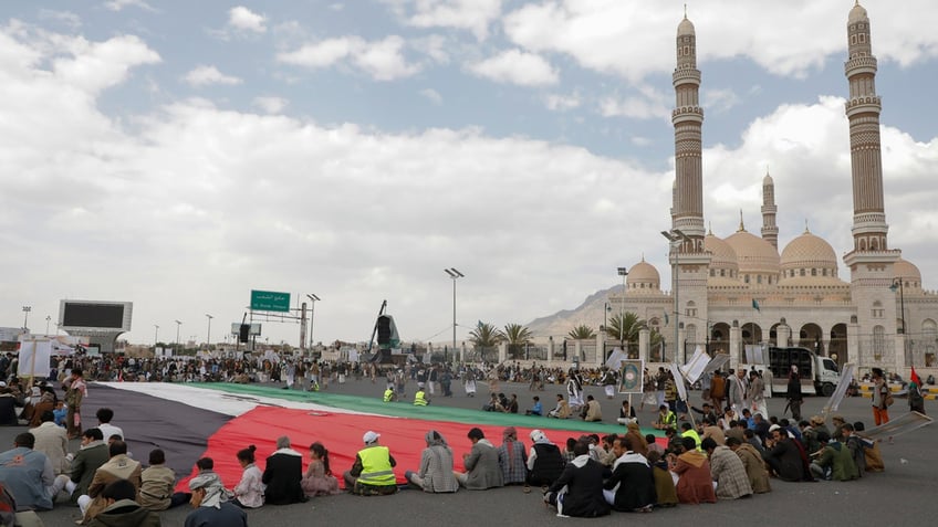 Houthi supporters sit in front of a giant Palestinian flag during a rally against the U.S.-led strikes against Yemen and in support of Palestinians in the Gaza Strip