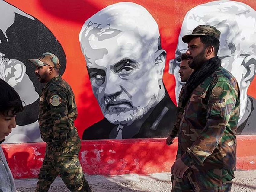 Members of the Popular Mobilization Forces walk past a graffitti depicting General Qassem