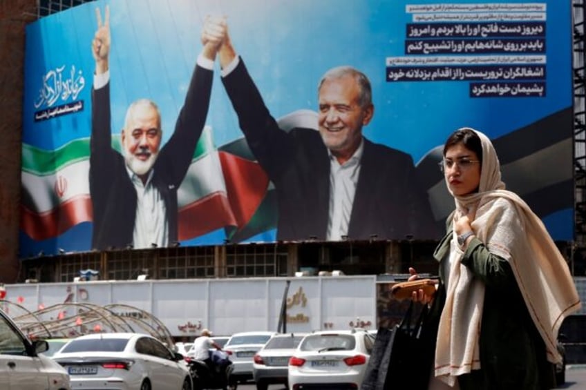 A woman walks past a picture of Iranian President Masoud Pezeshkian (R) and slain Hamas le