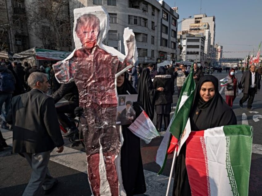 A veiled Iranian woman holds an Iran flag and stands next to an effigy of the U.S. Preside