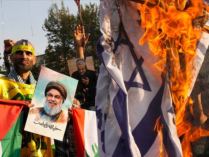 An Iranian demonstrator holds a poster of slain Hezbollah leader Hassan Nasrallah reading in Farsi: "Hezbollah is alive," as a representation of the Israeli flag is set on fire in an anti-Israeli gathering at Felestin (Palestine) Sq. in Tehran, Iran, Tuesday, Oct. 8, 2024. (AP Photo/Vahid Salemi)