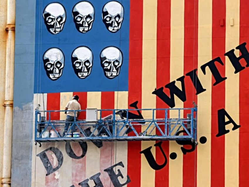 A man on a platform applies a fresh coat of paint to the landmark anti-US mural drawn on t