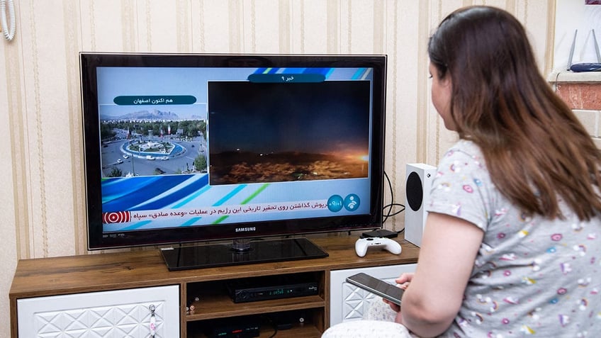 Iran woman watches TV following strikes