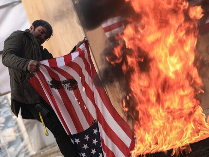 31 December 2021, Iraq, Baghdad: A man burns the US flag during a rally staged by supporte