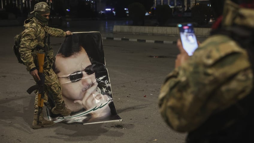 A Syrian opposition fighter takes a picture of a comrade stepping on a portrait of Syrian President Bashar Assad in Aleppo, early Saturday Nov. 30, 2024. (AP Photo/Ghaith Alsayed)