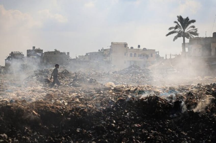 A Palestinian youth walks past piles of smouldering waste at Al-Maghazi Palestinian refuge