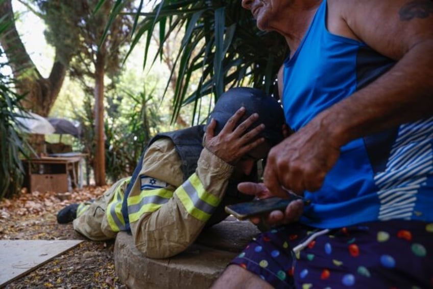 An Israeli firefighter and a resident take cover as sirens warn of rockets launched from s