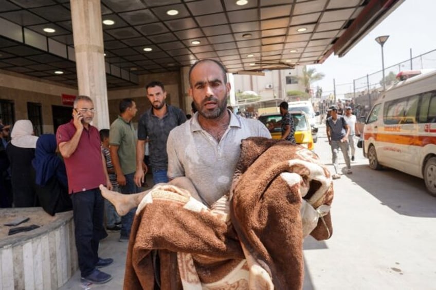 A man carries a child wrapped in a blanket at the Nasser hospital after Israeli strikes in