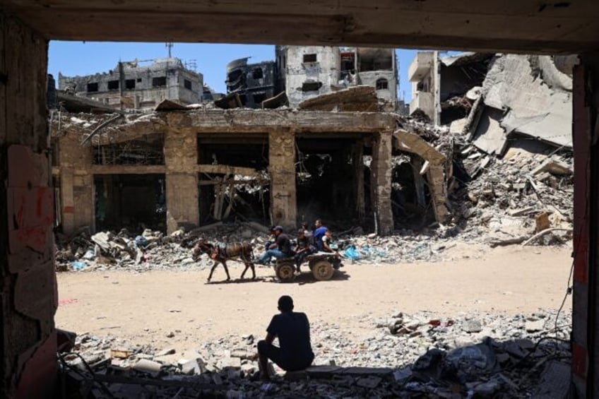 A man looks on as displaced Palestinians ride a donkey-pulled cart in Khan Yunis