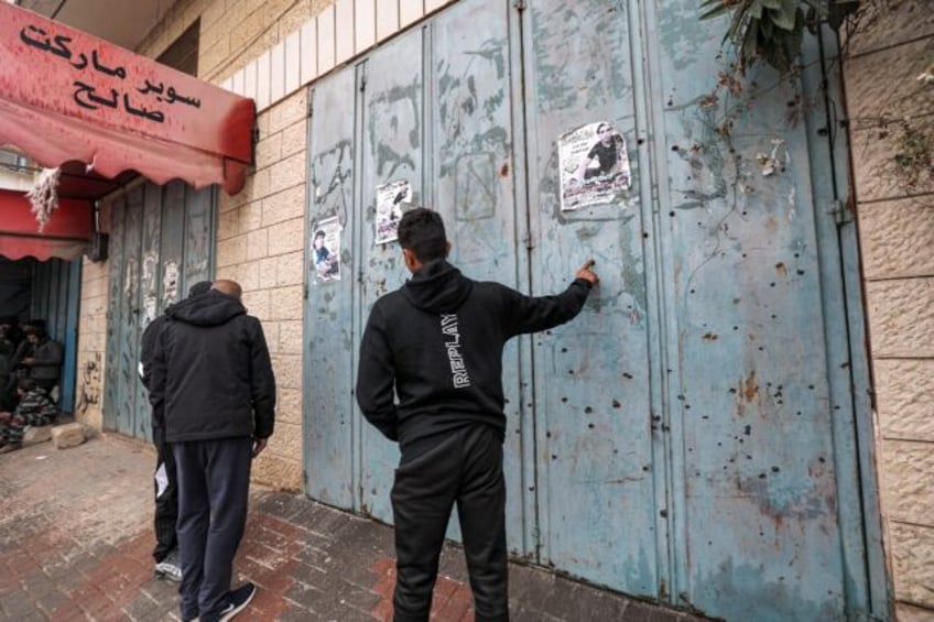 Palestinians inspect the bullet holes in the shutters of a shop in the West Bank town of Azzun after Israeli troops carried out a deadly raid