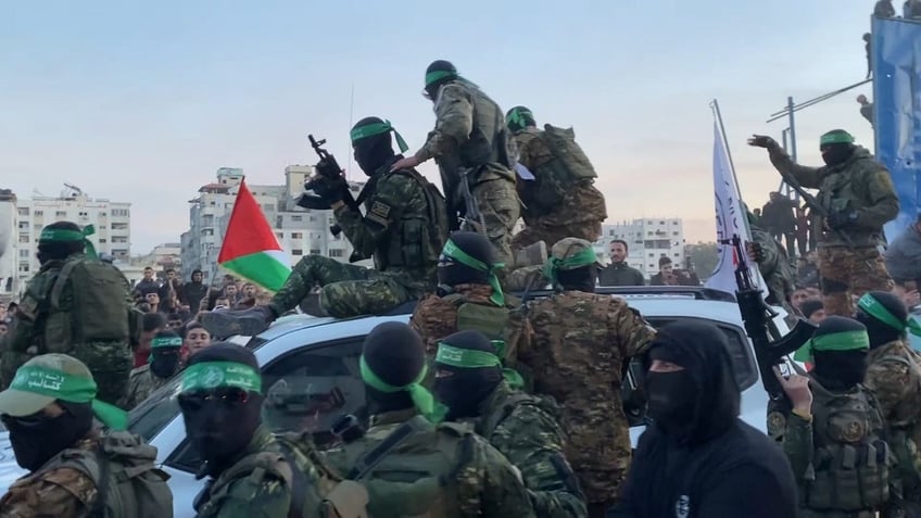 Hamas terrorists emerging from the shadows as they surround Red Cross vehicles.