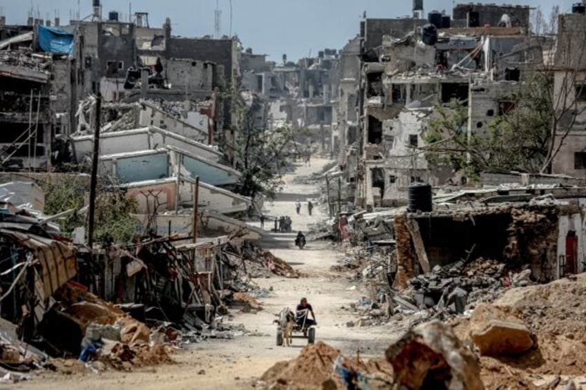 Palestinians walk on a road lined with destroyed buildings in Khan Yunis, where intense fi